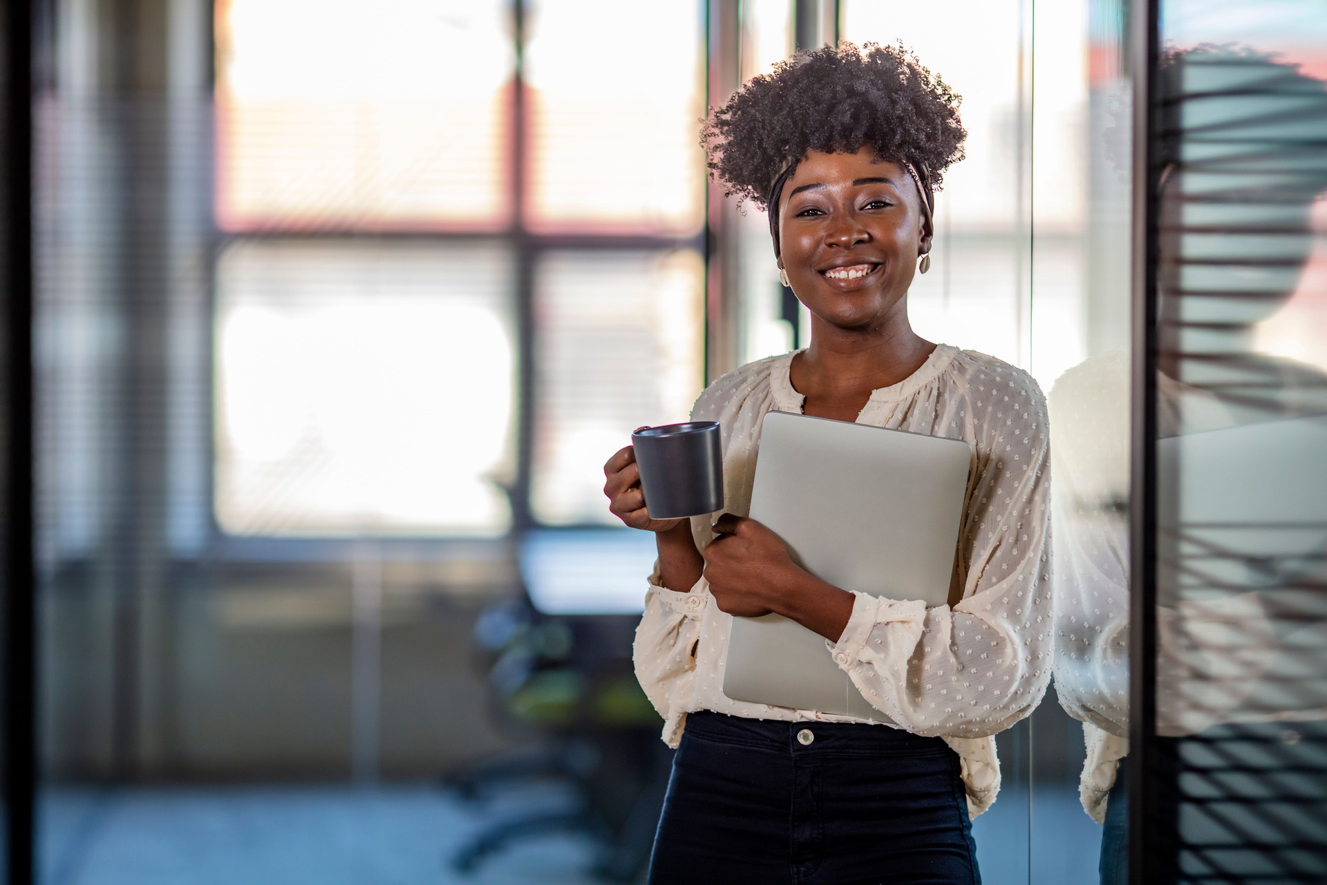 Pretty young dreamy African-American office worker standing with arms crossed and looking at camera.